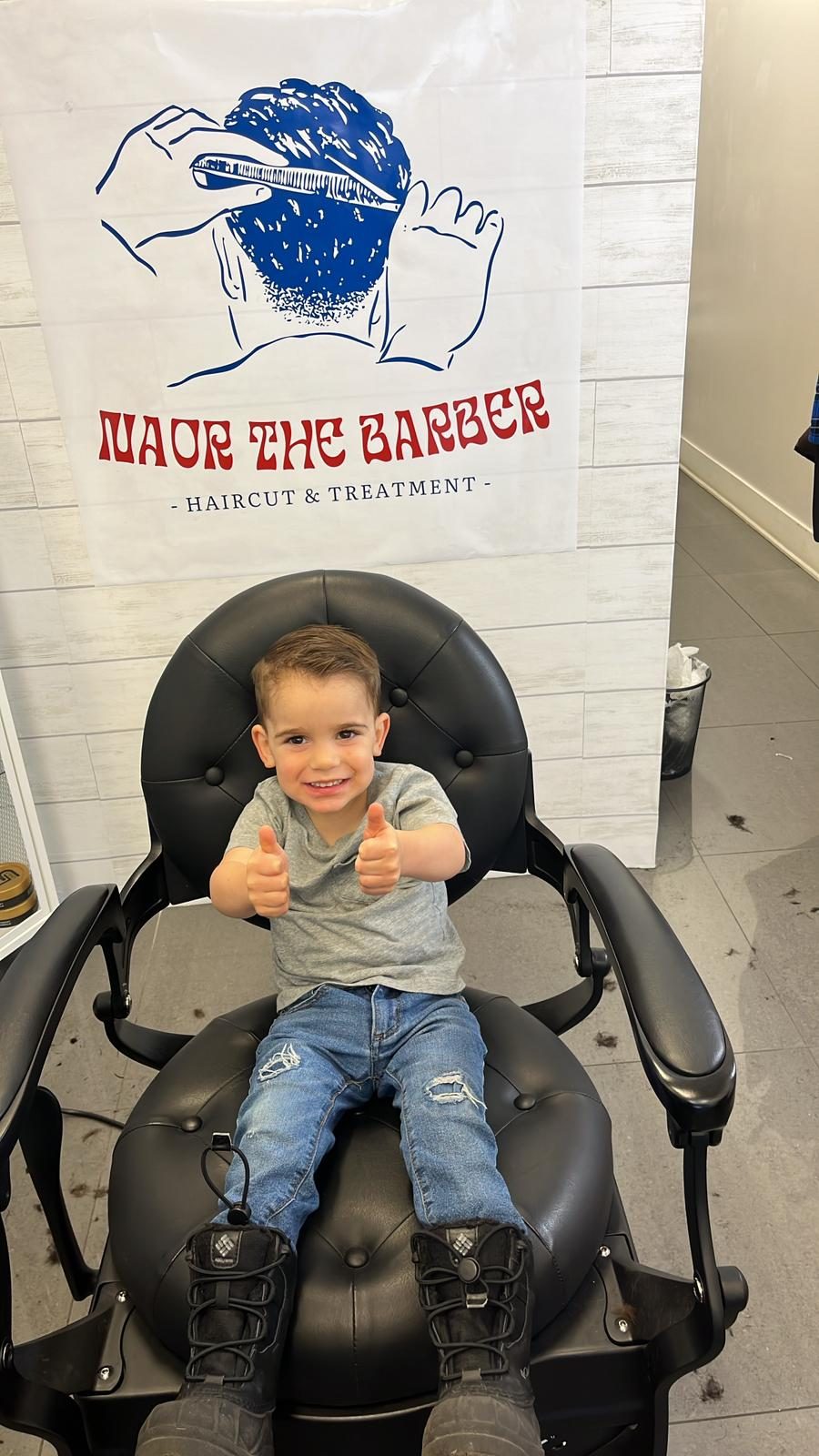Young boy giving two thumbs up in the barber chair after his kids haircut